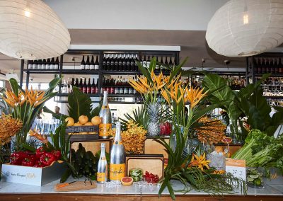 Champagne bottles display with flowers fruit vegetables Clicquot Beach Hut at Bondi Beach event